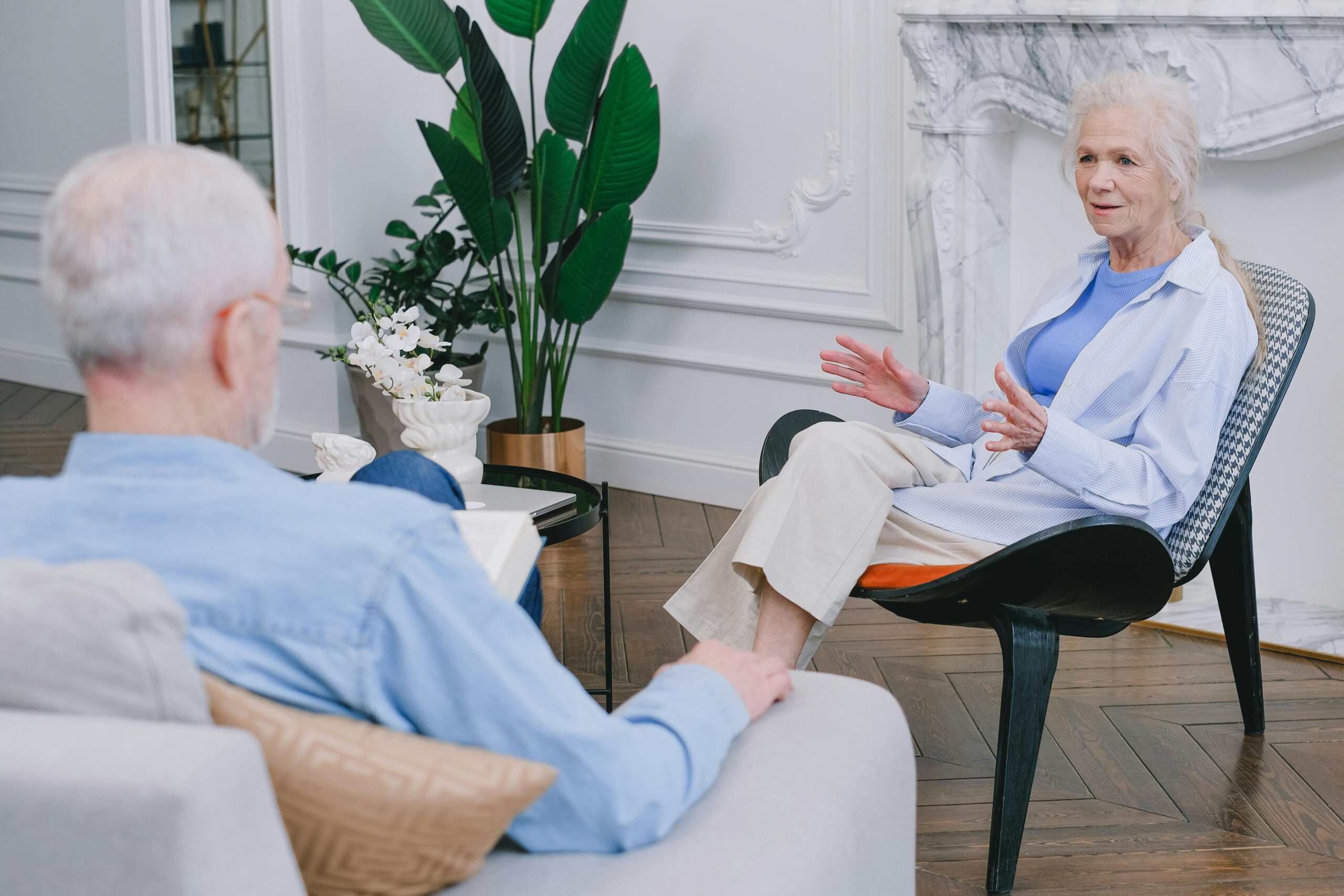 The Necessity of, and Resistance to, Old-Age Homes in Our Society Elderly couple discussing in a stylish living room with plants.