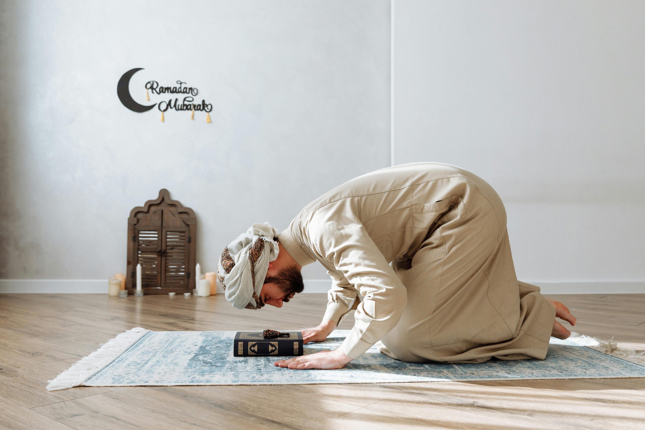 Prayer(Namaz/Salat) And Its Importance A man in traditional wear praying with Quran during Ramadan indoors.