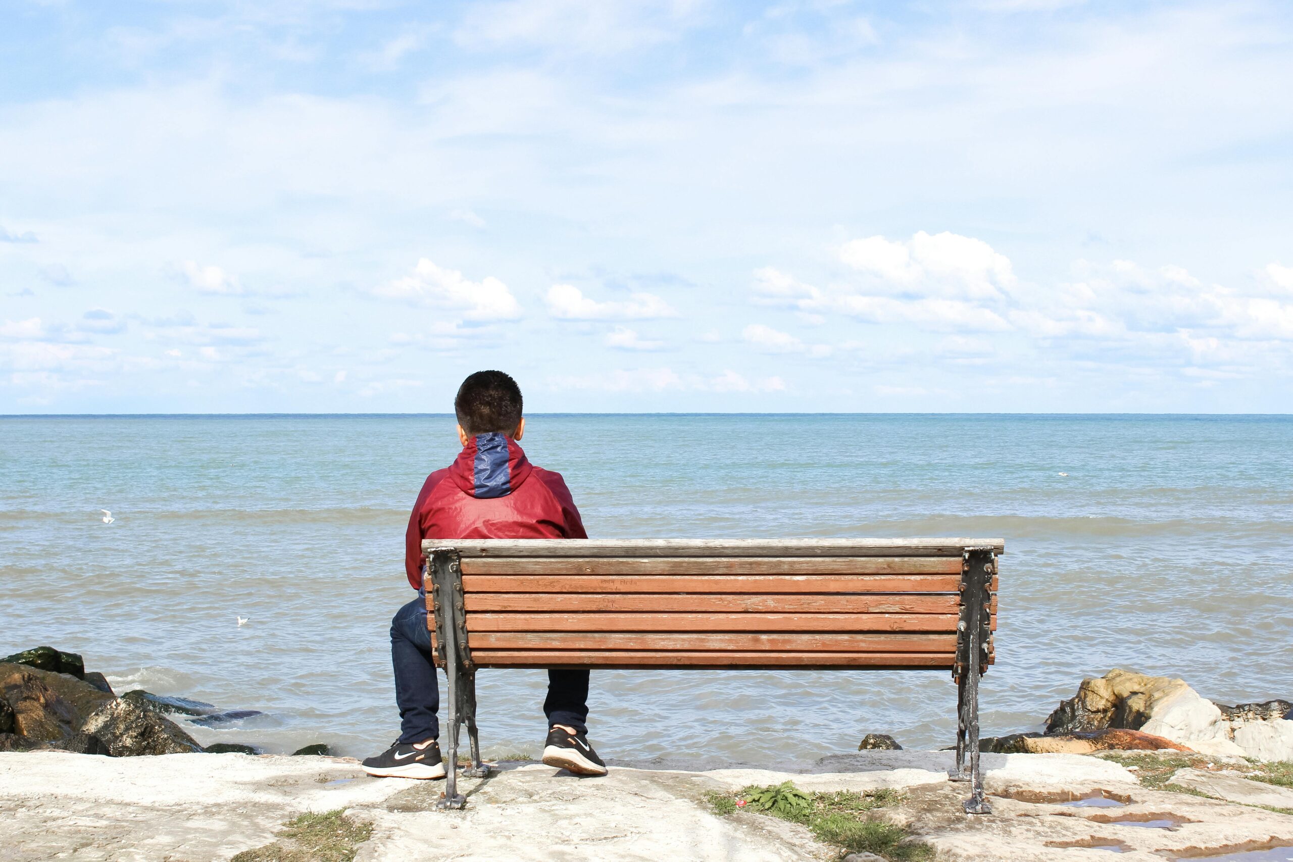 A child sitting on a bench gazing at the sea on the Ünye coast, Ordu, Türkiye.