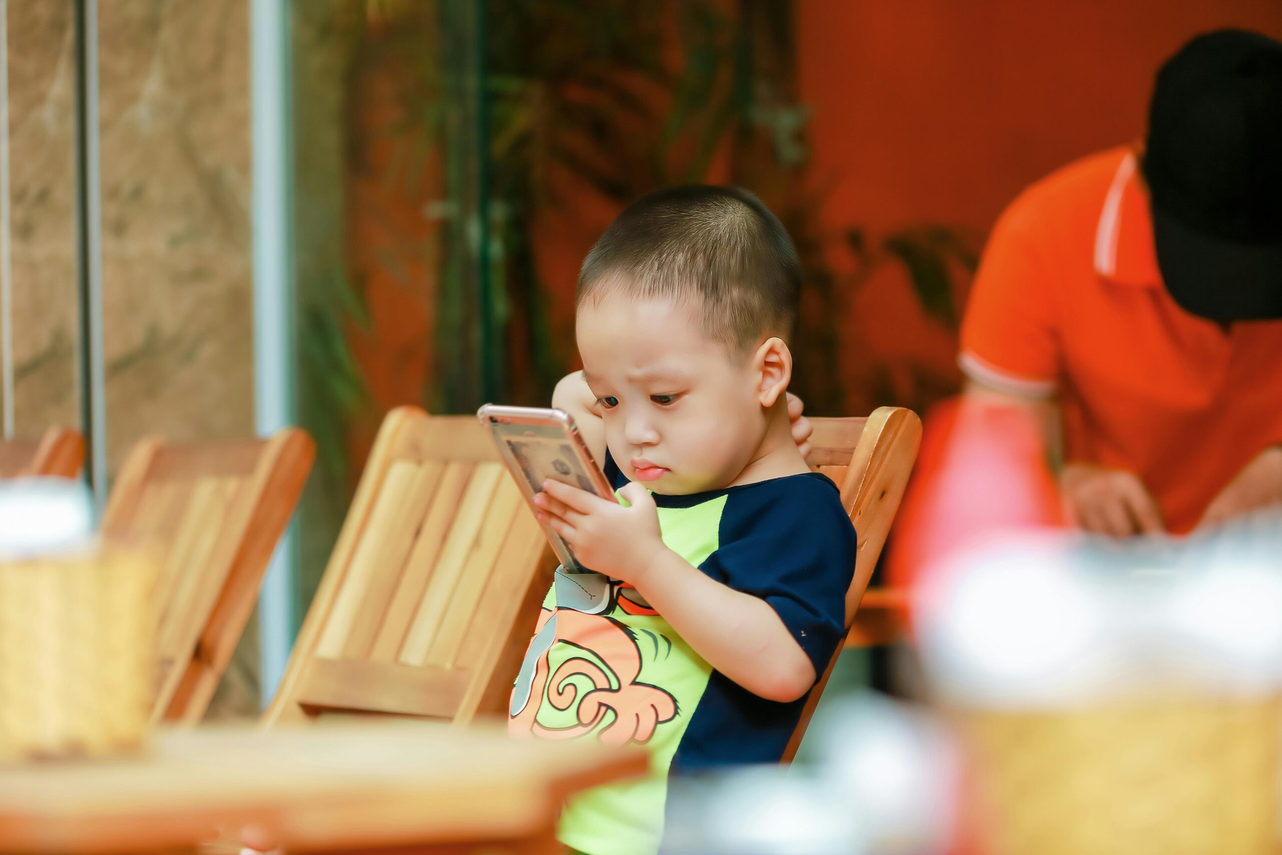 A young child focused on a smartphone while sitting indoors, highlighting modern technology in leisure time.